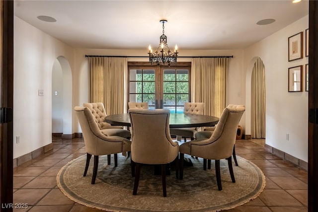 dining area featuring a chandelier, arched walkways, tile patterned flooring, and baseboards