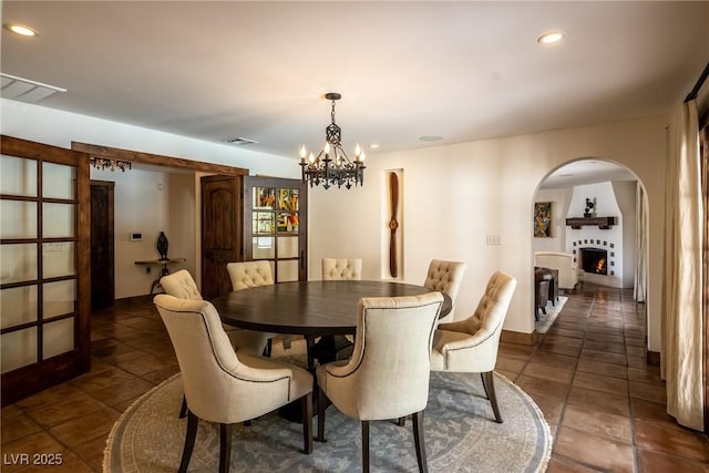 dining room with arched walkways, a chandelier, dark tile patterned floors, recessed lighting, and a lit fireplace
