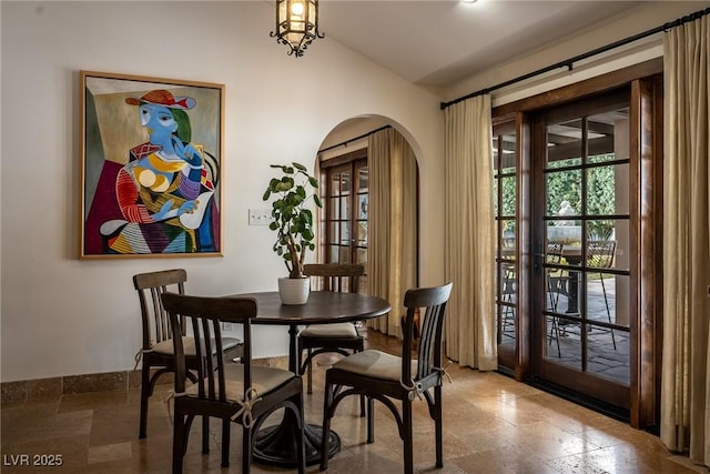 dining room with lofted ceiling, arched walkways, and stone tile floors