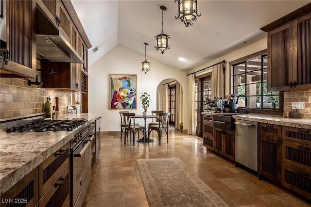 kitchen featuring appliances with stainless steel finishes, wall chimney range hood, arched walkways, lofted ceiling, and decorative backsplash