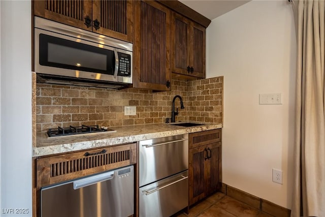 kitchen with stainless steel appliances, a sink, decorative backsplash, tile patterned floors, and dark brown cabinetry