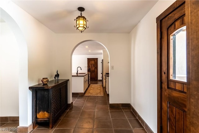 corridor featuring a sink, arched walkways, dark tile patterned floors, and baseboards