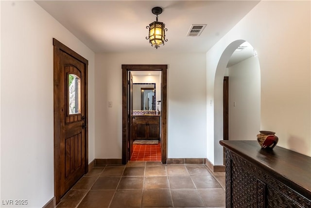 hall with baseboards, dark tile patterned flooring, and arched walkways