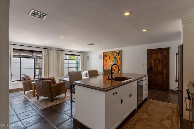 kitchen featuring a sink, appliances with stainless steel finishes, dark countertops, white cabinetry, and a center island with sink