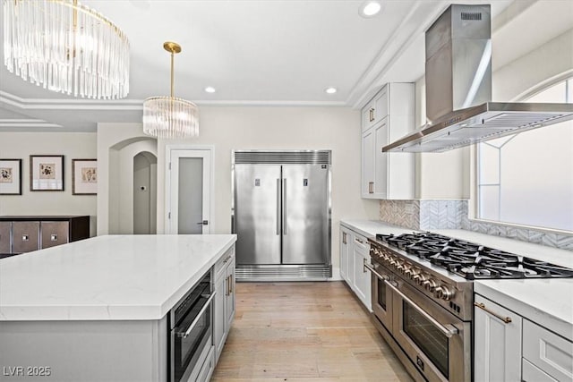 6335 Mount Eden Ave, Las Vegas, NV 89139 - kitchen with high quality appliances, wall chimney exhaust hood, a chandelier, a kitchen island, and light wood-style floors