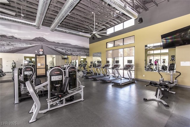 exercise room featuring baseboards, ceiling fan, a healthy amount of sunlight, and a towering ceiling