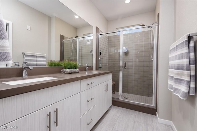 bathroom with a shower stall, double vanity, baseboards, and a sink
