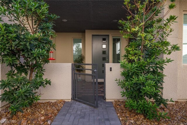 doorway to property with a gate, stucco siding, and fence