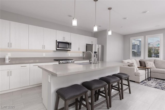 kitchen featuring light countertops, appliances with stainless steel finishes, a sink, open floor plan, and a kitchen breakfast bar