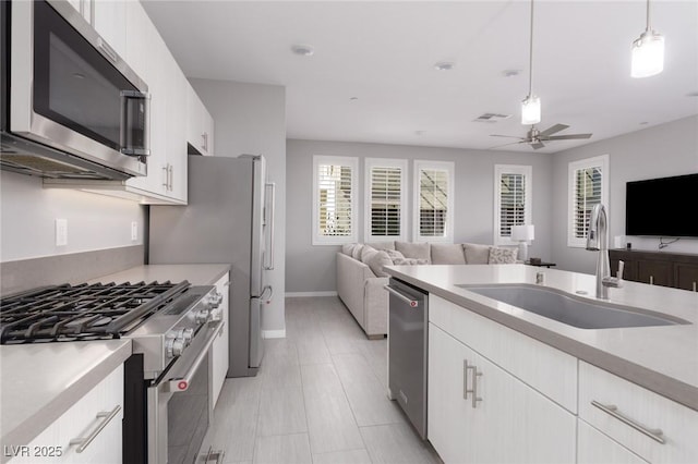 kitchen featuring open floor plan, light countertops, a sink, a ceiling fan, and appliances with stainless steel finishes
