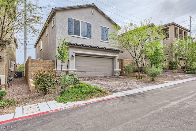 traditional home with central AC, a garage, stucco siding, and decorative driveway