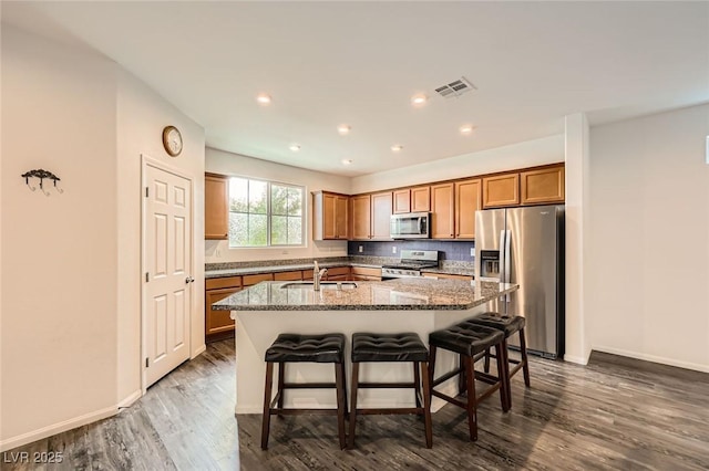 kitchen featuring visible vents, a sink, a kitchen island with sink, brown cabinets, and stainless steel appliances