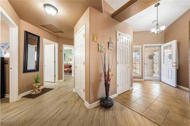 entrance foyer with light wood finished floors, baseboards, an inviting chandelier, and lofted ceiling