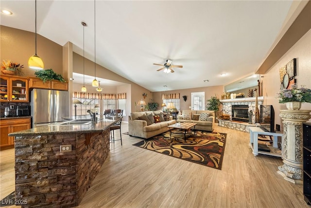 living room with light wood-type flooring, ceiling fan, lofted ceiling, and a stone fireplace
