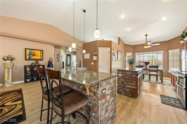 kitchen featuring lofted ceiling, light wood-type flooring, an island with sink, ceiling fan, and a sink