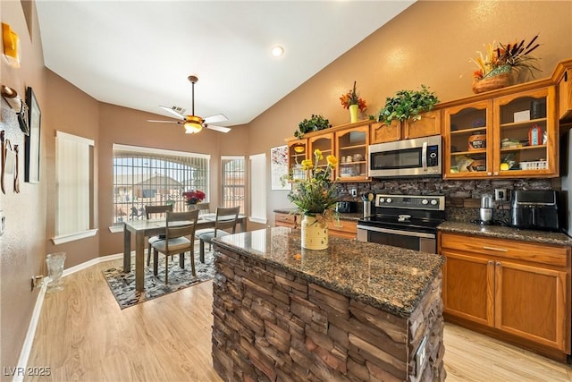 kitchen with glass insert cabinets, light wood-style flooring, brown cabinets, ceiling fan, and stainless steel appliances