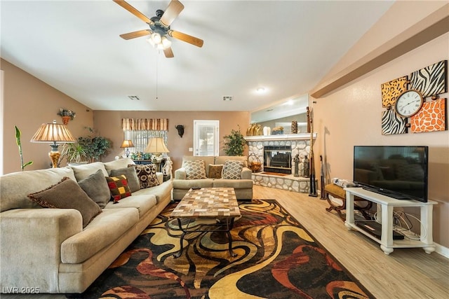 living room with a stone fireplace, visible vents, ceiling fan, and wood finished floors