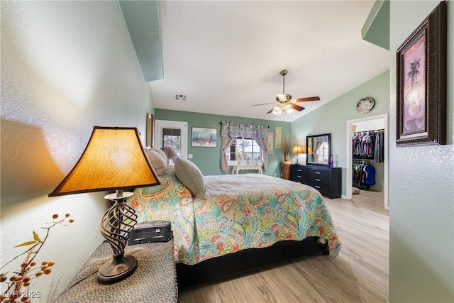 bedroom featuring vaulted ceiling, a walk in closet, visible vents, ceiling fan, and wood finished floors