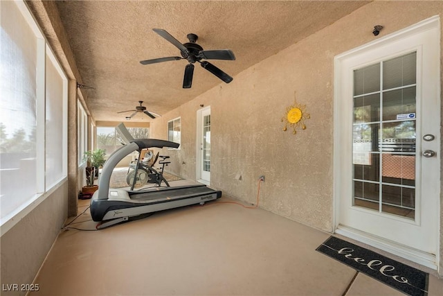 exercise area featuring a ceiling fan, a textured wall, and a textured ceiling