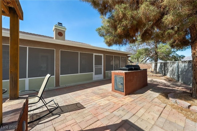 view of patio with a grill, fence, a sunroom, and an outdoor kitchen