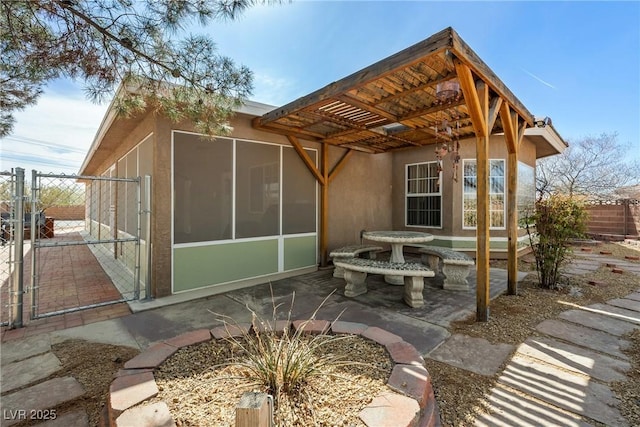 back of house featuring a sunroom, stucco siding, a patio, fence, and a gate
