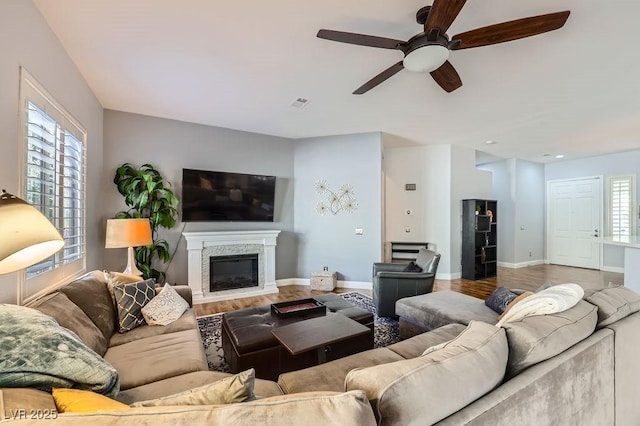 living room featuring ceiling fan, a glass covered fireplace, visible vents, wood finished floors, and baseboards