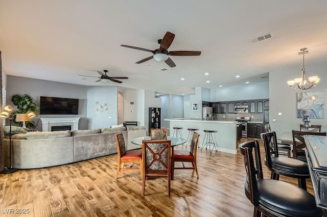 dining area with visible vents, light wood-style floors, a fireplace, recessed lighting, and ceiling fan with notable chandelier