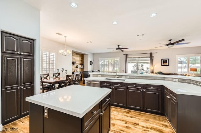 kitchen with a sink, light countertops, a center island, and ceiling fan with notable chandelier