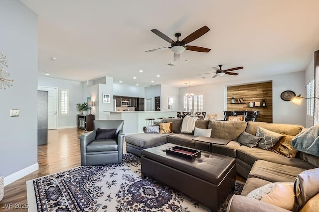 living area with light wood-style floors, ceiling fan with notable chandelier, baseboards, and recessed lighting