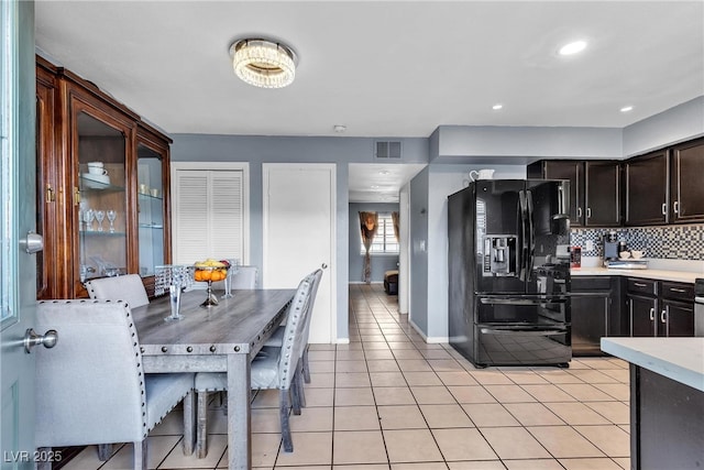 kitchen with light countertops, backsplash, light tile patterned floors, baseboards, and black fridge
