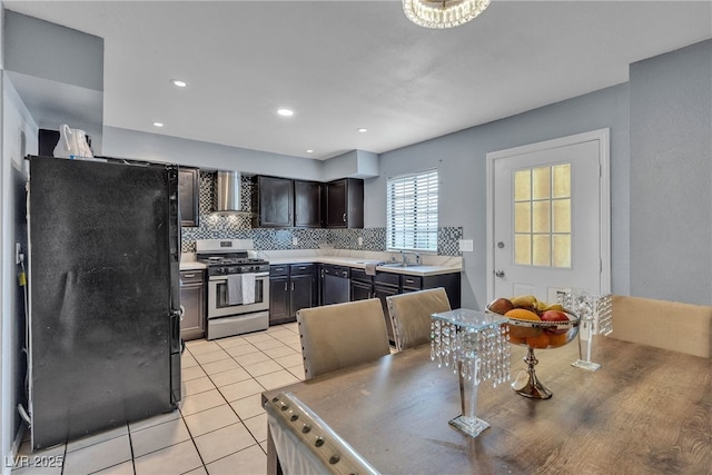 kitchen with light tile patterned floors, freestanding refrigerator, wall chimney exhaust hood, gas range, and tasteful backsplash