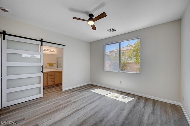 unfurnished bedroom with a barn door, wood finished floors, visible vents, a ceiling fan, and baseboards