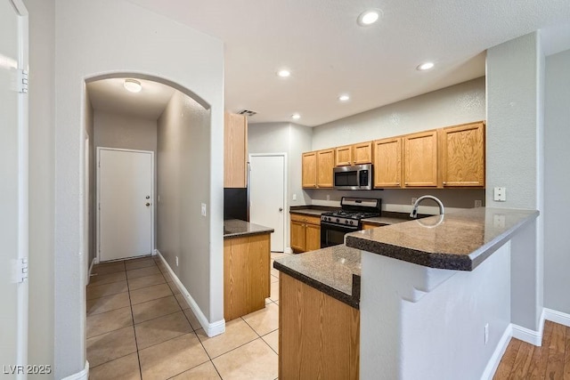 kitchen with a peninsula, arched walkways, recessed lighting, stainless steel microwave, and gas range oven