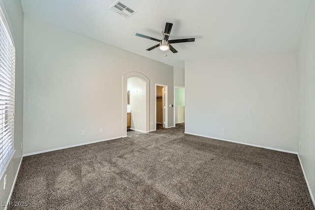 empty room featuring ceiling fan, arched walkways, visible vents, dark colored carpet, and baseboards