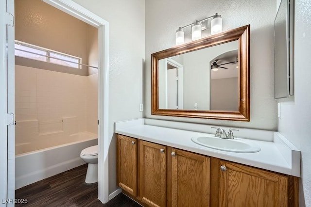 full bath with washtub / shower combination, toilet, ceiling fan, vanity, and wood finished floors