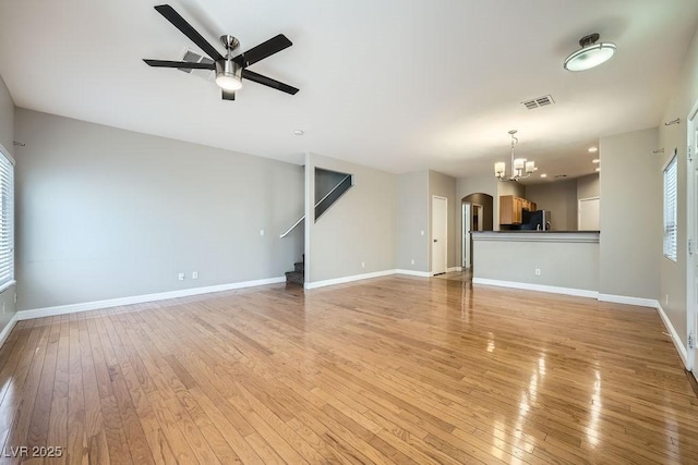 unfurnished living room with visible vents, baseboards, light wood-type flooring, ceiling fan with notable chandelier, and stairs