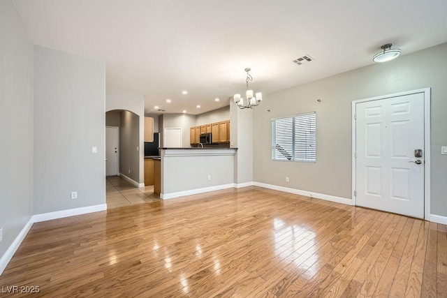 unfurnished living room featuring a notable chandelier, baseboards, light wood-style floors, visible vents, and arched walkways