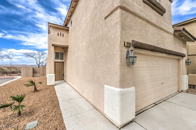 view of side of home featuring stucco siding, fence, and concrete driveway