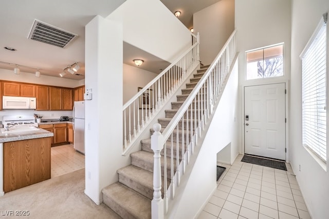 entryway with rail lighting, stairs, baseboards, a high ceiling, and visible vents