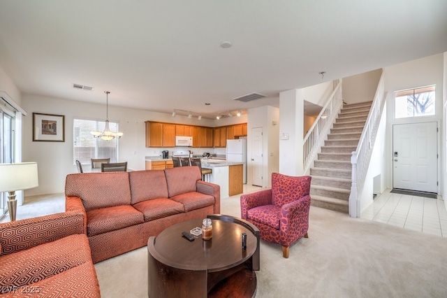 living area with visible vents, a chandelier, rail lighting, stairway, and light colored carpet