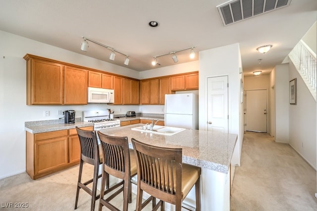 kitchen with a kitchen breakfast bar, white appliances, a sink, visible vents, and a kitchen island with sink
