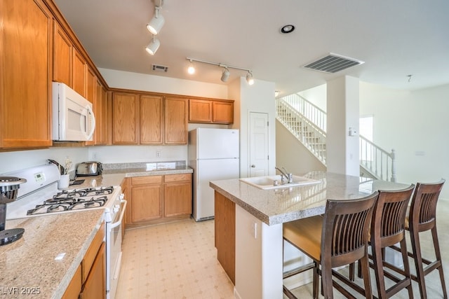 kitchen featuring an island with sink, a sink, light floors, white appliances, and visible vents