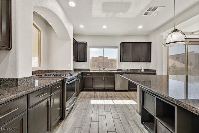 9830 Wild Coyote Ct, Las Vegas, NV 89141 - kitchen featuring appliances with stainless steel finishes, dark stone counters, dark brown cabinetry, recessed lighting, and light wood finished floors