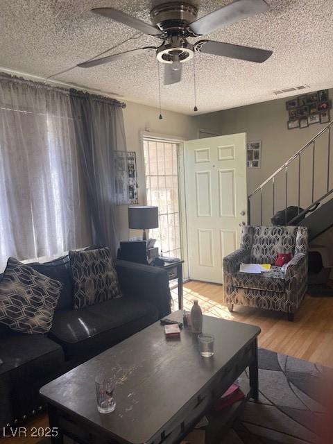 living area with visible vents, ceiling fan, light wood-type flooring, and a textured ceiling
