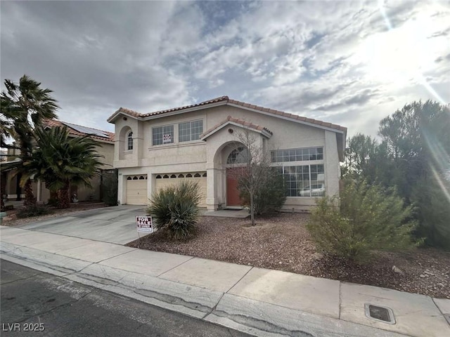 mediterranean / spanish-style home with driveway, an attached garage, a tiled roof, and stucco siding