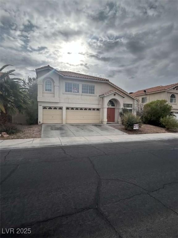 mediterranean / spanish-style home featuring driveway, stucco siding, a tile roof, and an attached garage