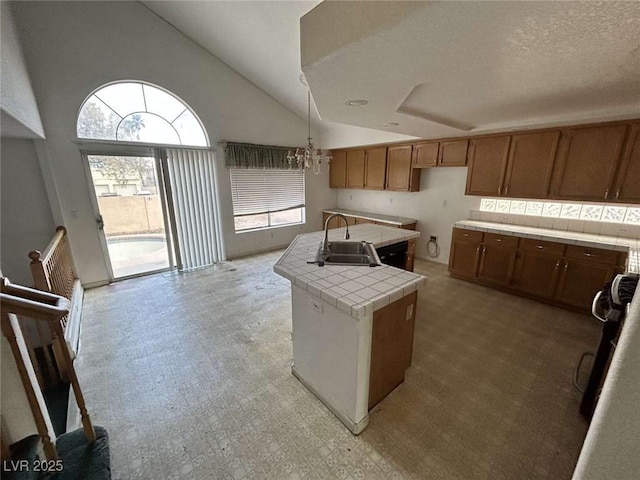 kitchen with a chandelier, a sink, tile countertops, an island with sink, and light floors