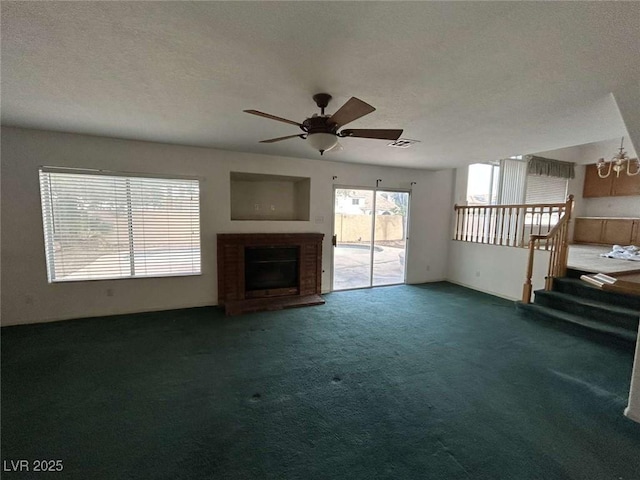 unfurnished living room featuring carpet flooring, a textured ceiling, visible vents, a fireplace, and ceiling fan with notable chandelier
