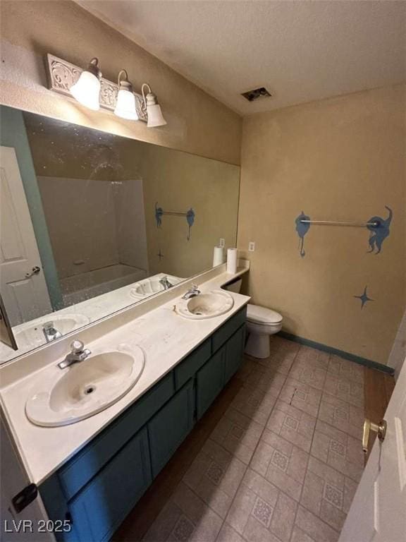 bathroom featuring toilet, a sink, double vanity, and baseboards