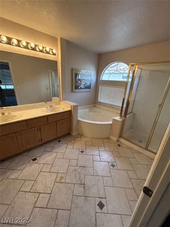 full bath featuring a shower stall, a textured ceiling, a sink, double vanity, and a bath